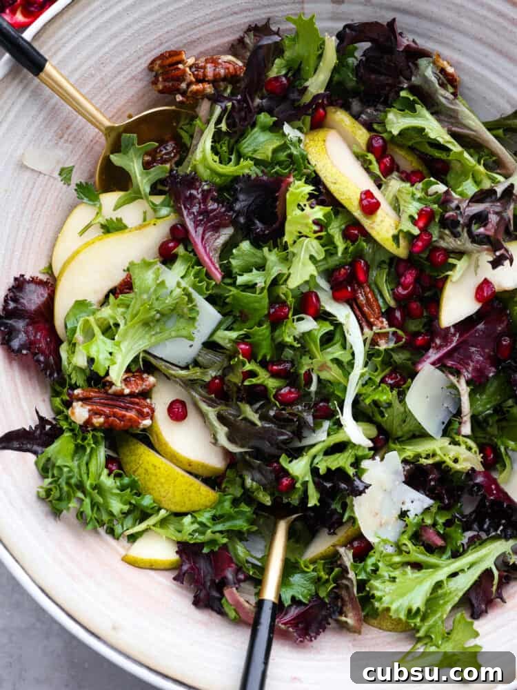 A close up top view of a pomegranate salad with gold tongs.