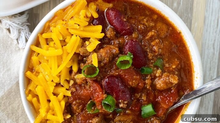 overhead shot of chili in a bowl garnished with green onion and cheese with cornbread on the side