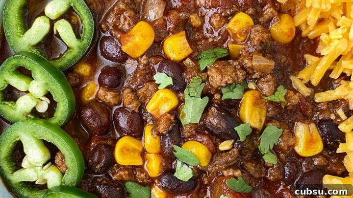 close up of chorizo beef chili in a white bowl garnished with sliced jalapeno, cheese and cilantro