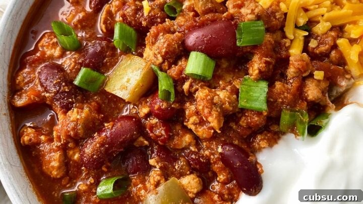 cooked turkey chili in a white bowl topped with cheese, green onion and sour cream with a silver spoon