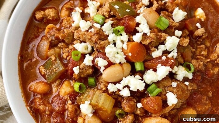 overhead shot of Cooker Buffalo Chicken Chili in a white bowl garnished with blue cheese and green onion