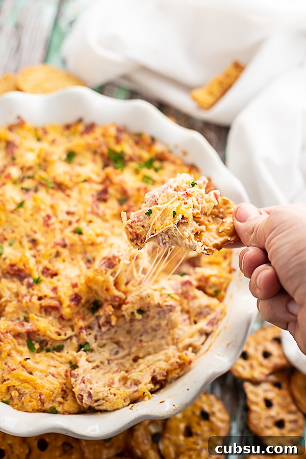 Reuben dip in a white ruffled pie dish with a pretzel chip being dipped in