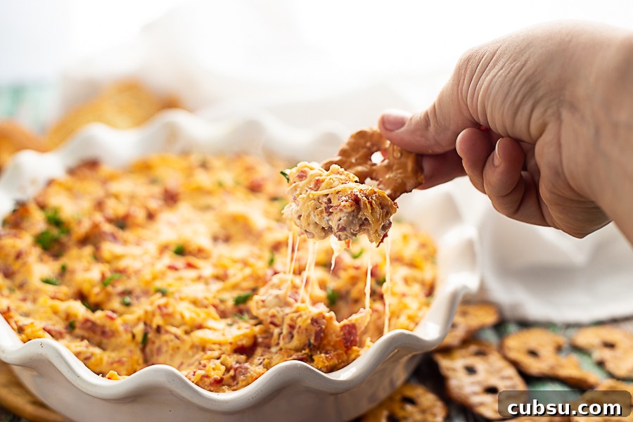 Reuben dip in a white ruffled pie dish with a pretzel chip being dipped in