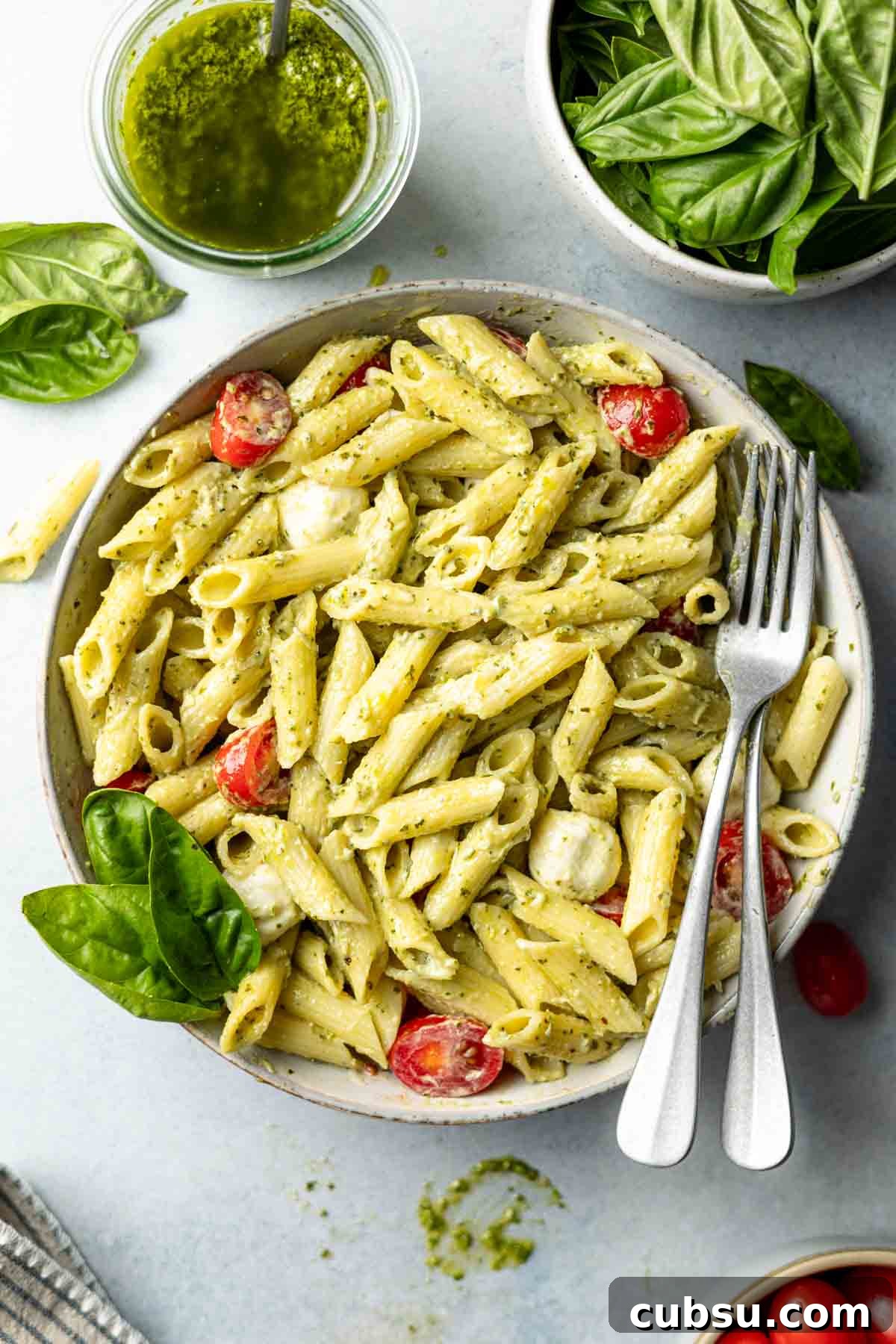 Pasta in large bowl tossed with creamy pesto sauce, tomatoes, and fresh mozzarella.