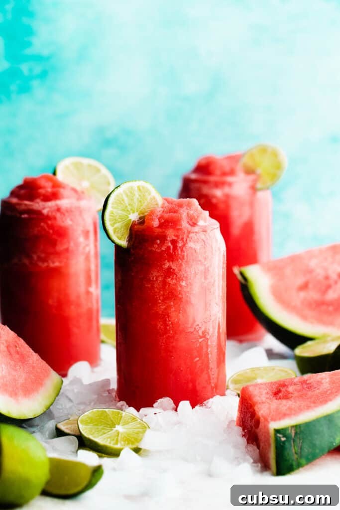 Three glasses of frozen watermelon margaritas surrounded by ice and topped with lime slices.