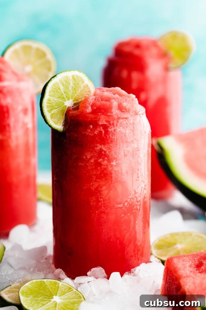 A close-up of a glass of bright pink frozen watermelon margarita topped with a lime slice.