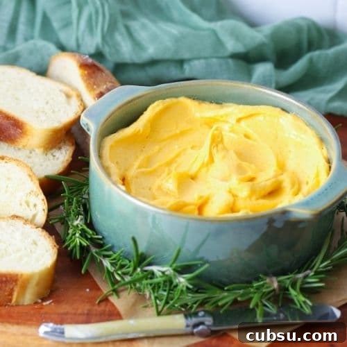 Cheddar butter being served in a bowl on a serving board with slices of sourdough bread.