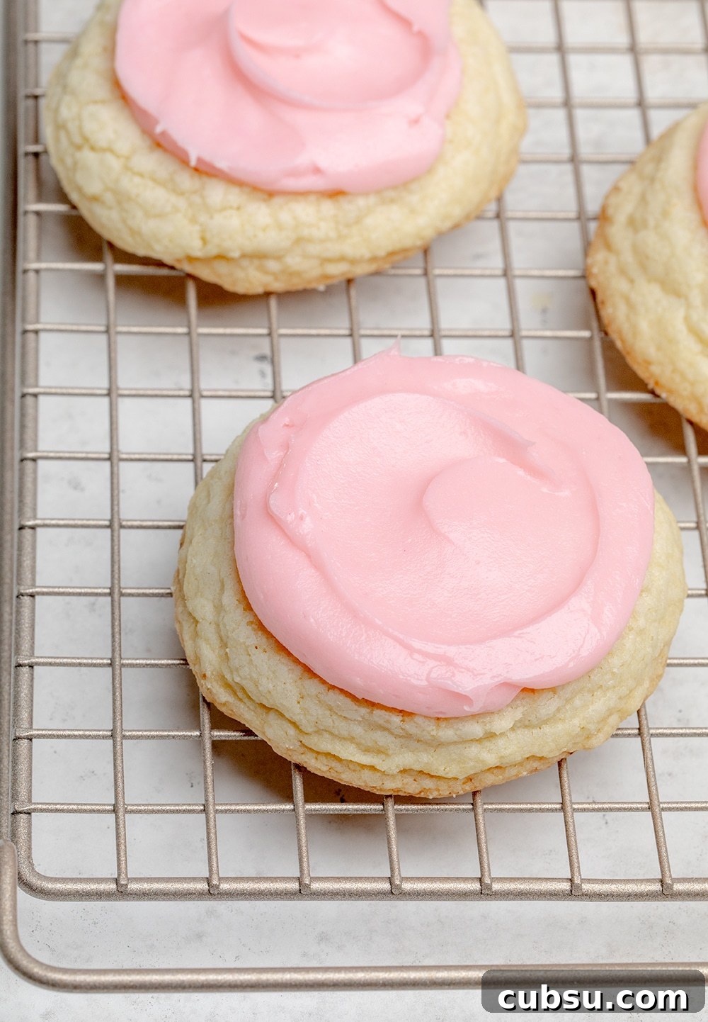light yellow cookies with pink frosting on wire rack overhead