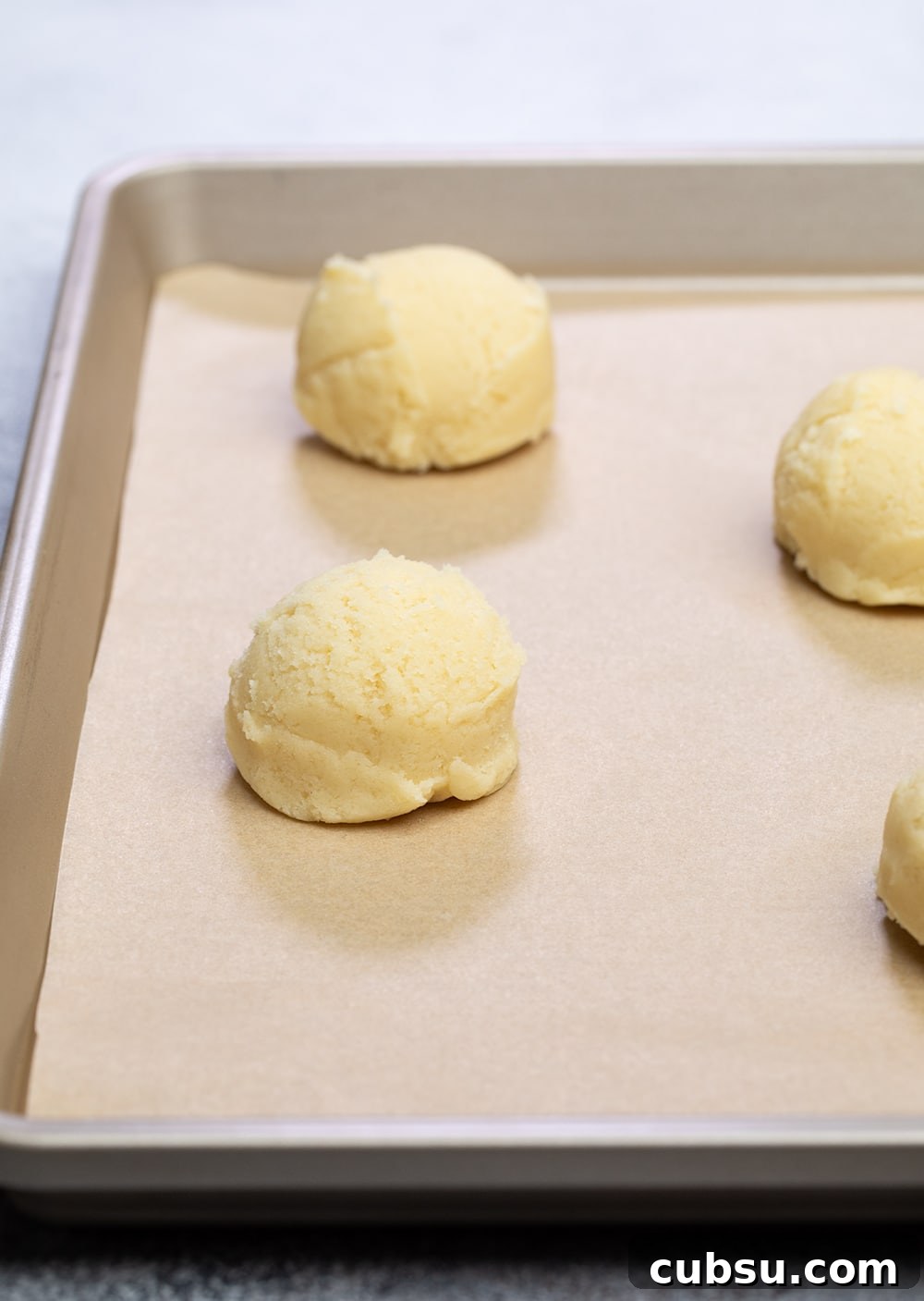 closeup image of round mounds of light yellow cookie dough on a baking sheet