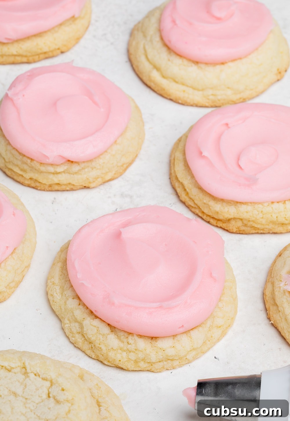 Closeup image of pink swirled frosting on top of round yellow cookie with pastry bag with pink frosting