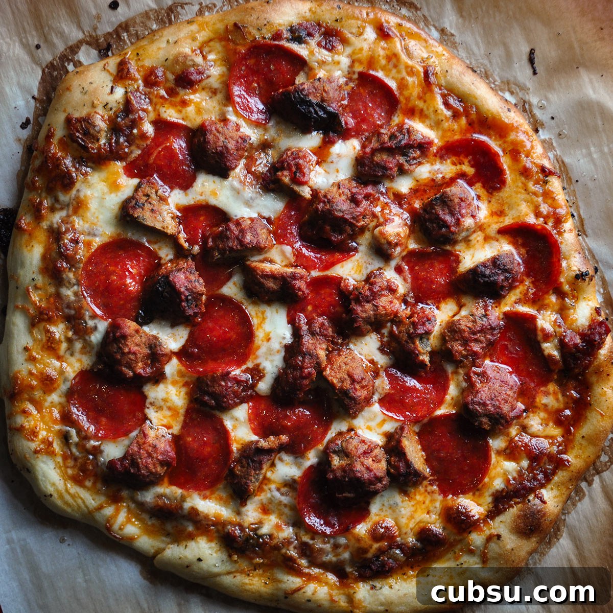 A homemade pepperoni and meatball pizza that's been baked on parchment paper.
