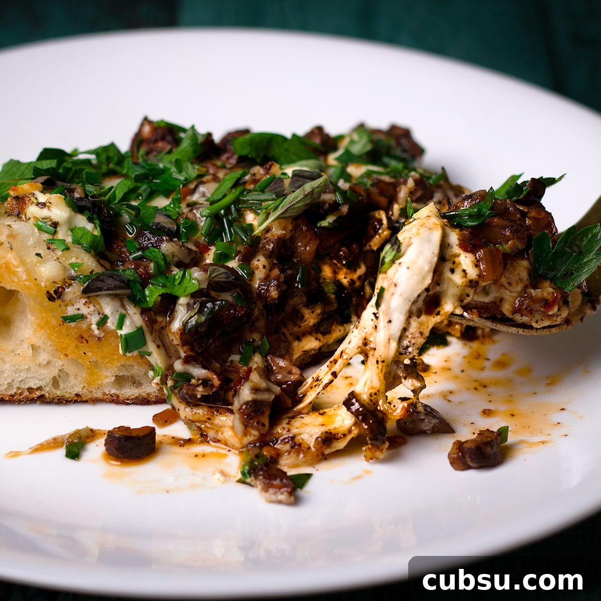 Using a fork to cut a bite of mushroom pizza from a slice on a white plate.