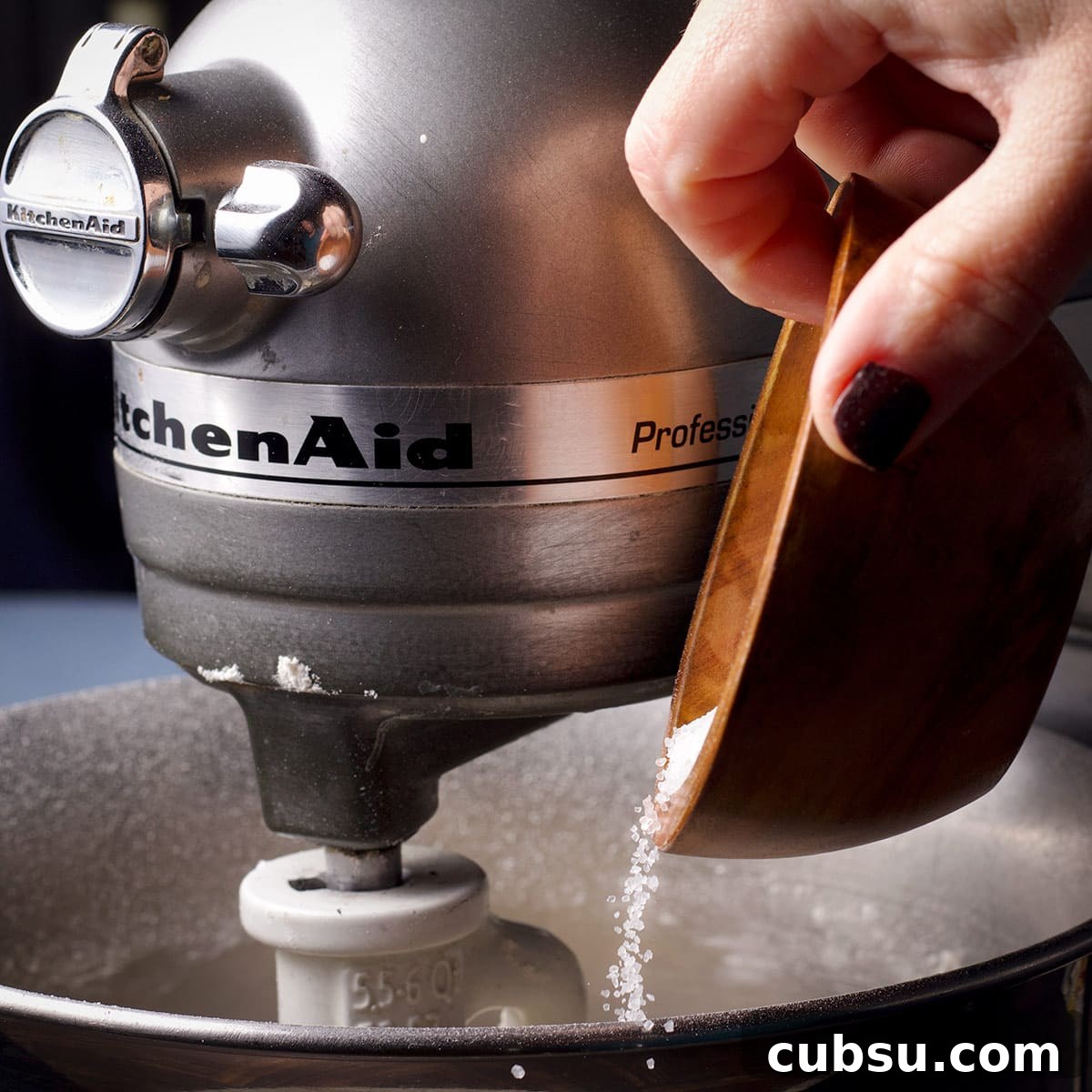 Adding salt to pizza dough while it mixes in the bowl of a stand mixer.